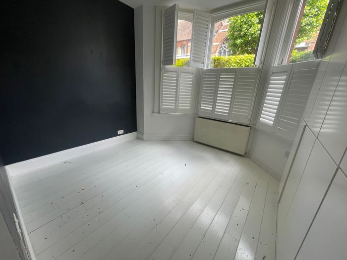 Empty bedroom with navy accent wall and bay window shutters, before styling