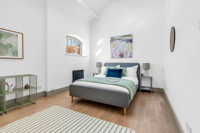 Same room staged with a grey upholstered bed and artwork